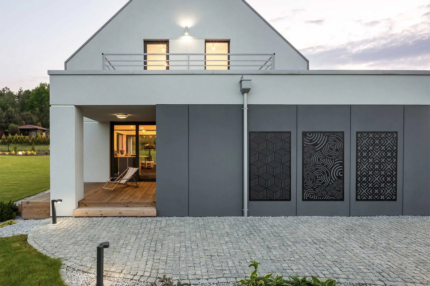Modern white house with black decorative panels and cobblestone driveway.