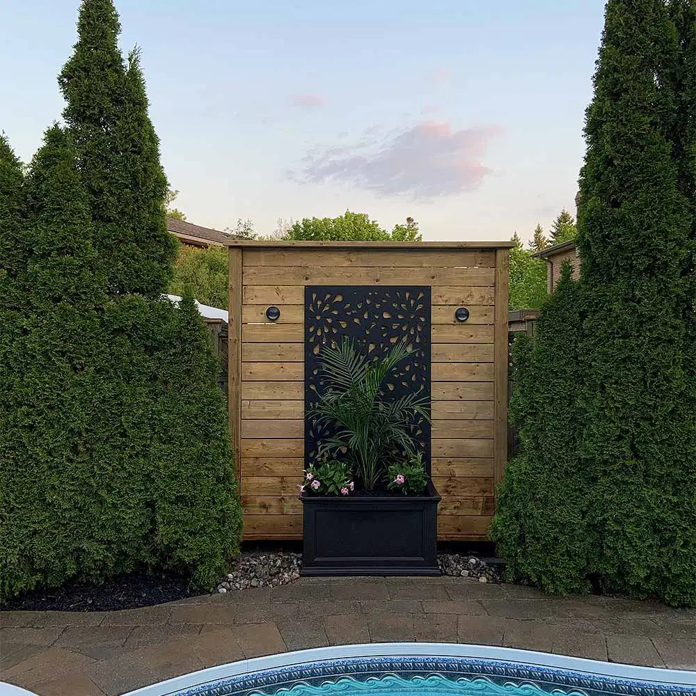 Wooden garden shed with black metal door and decorative cutout design, dark blue planter box.