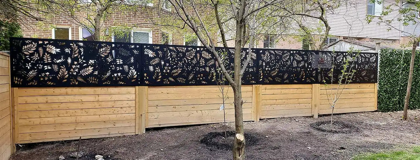 Wooden privacy fence with black metal decorative panels featuring leaf patterns.